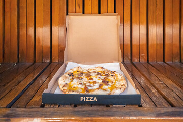 Pizza in takeaway box on wooden bench