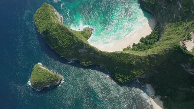 Aerial drone shot in the iconic Kelingking Beach, the 'T-Rex' shaped headland, and the towering limestone cliffs of Nusa Penida. Turquoise Indian Ocean crashes against the rocks and white-sand beach.