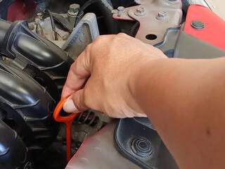 Car service. Close-up of a mechanic's hand holding an oil dipstick, checking engine oil levels in a...