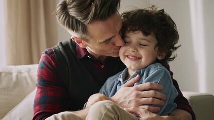 Father lovingly hugging and kissing his happy young son at home, showing warmth, affection, and family connection.
