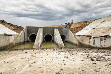 Construction workers develop a stormwater drainage system at a rural site. Heavy machinery is used while cloudy skies appear overhead, indicating possible rain