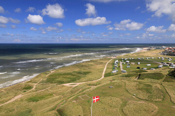 Landscape photo with a view of the green hills and North Sea coast with the Danish flag in the foreground near Hirtshals in Denmark 