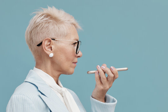 Middle-aged woman using voice assistant on her smartphone side view horizontal shot