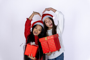 Two girls wearing Santa hats are holding Christmas presents and making a heart.