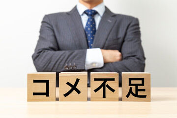 「コメ不足」と書かれたブロックと腕組みをするビジネスマン