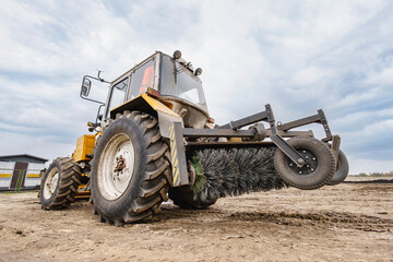 A tractor uses a brush attachment to clear mud and debris from a farm field, showcasing the machinery's function in agricultural maintenance
