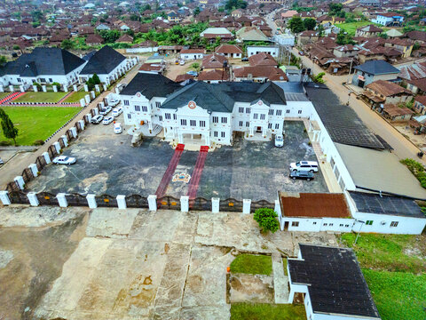 Aerial view of a grand building with white walls and dark roofs, complemented by red carpet and parked cars, amidst lush greenery, Ile-Ife, Osun, Nigeria.