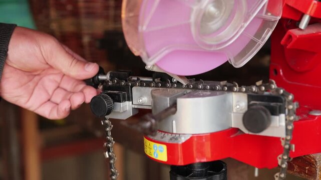 A person sharpens a chain with a power tool in a workshop, surrounded by tools. Sparks fly as the blade makes contact, highlighting craftsmanship and safety