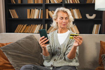 Happy middle aged woman shopping online with smartphone paying with credit card. Mature lady buying on Internet enter credit card details at home indoors. Online shopping delivery service ecommerce