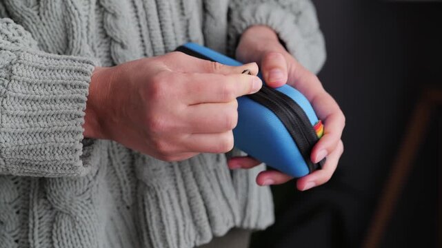 A person is gently holding a blue zipper case in their hands, dressed in a warm knitted sweater, surrounded by a comfortable indoor environment