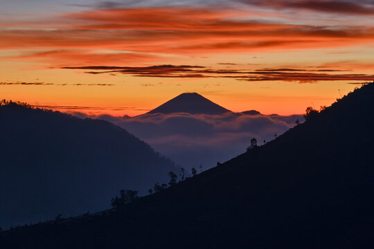 View of the majestic, silhouetted mountains loom under a fiery dawn sky painted with vivid oranges and yellows, creating a serene landscape, Banjarnegara, Central Java, Indonesia.