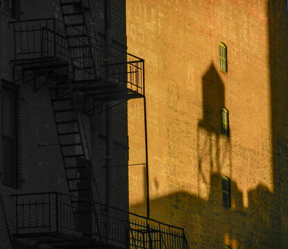View of sun-drenched brick buildings casting shadows, a fire escape clinging to one side, creating a study in contrasts and urban geometry, New York, New York, United States.