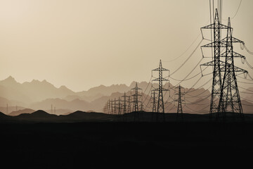 Silhouette of power lines at  dusk in the sandy desert against the background of mountain layers,...