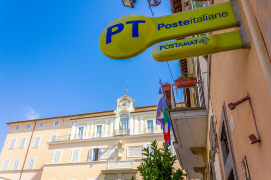 Castel Gandolfo, Italy - June 21, 2025: Poste Italiane (Italian Post) and Postamat sign outside a post office in Castel Gandolfo, Italy, with the historic Palazzo Pontificio in the background. 