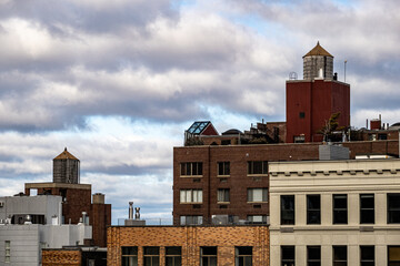 View of rooftops in a dense urban landscape, where brick buildings and water towers stand against a backdrop of a cloudy sky, New York, USA.