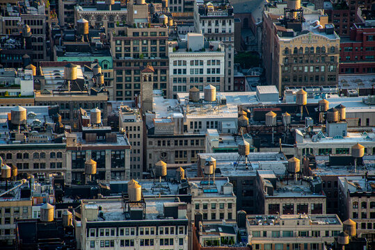 View of rooftops peppered with wooden water tanks bask in the soft glow of sunset, creating a captivating contrast against the urban skyline, New York, New York, United States.