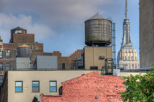 View of weathered water towers stand stark against the city skyline, with the iconic Empire State Building piercing the sky, a blend of old and new, New York, New York, United States.
