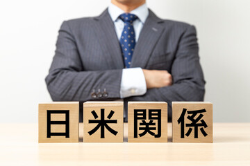 「日米関係」と書かれたブロックと腕組みをするビジネスマン