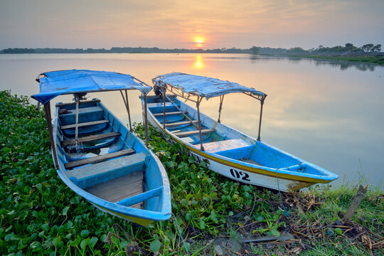 View of two vibrant blue boats rest on the verdant shore as the sun casts a golden glow over the tranquil lake, Boyolali, Central Java, Indonesia.
