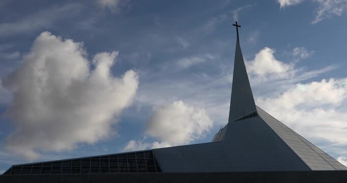 Contemporary Methodist Church in Tallinn, Estonia&mdash;a tall white spire with a cross rises into blue sky and sculpted clouds. Serene spiritual mood, modern minimalist design.