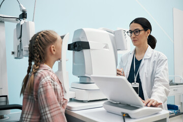 Caucasian female optometrist examining Caucasian girl using ophthalmology equipment in medical...