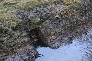 Freshly dug drainage ditch with visible cast iron outflow covers
