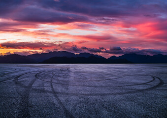 Empty asphalt race track with tire skid marks and mountain landscape at sunset