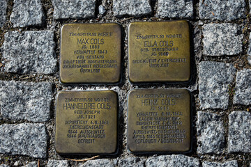 Four brass Stolpersteine (stumbling blocks) set into a Berlin cobblestone sidewalk. This public art project by Gunter Demnig memorializes the victims of the Holocaust, including the Cohn/Cols family.