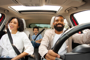 Joyful Black family riding car singing and having fun during road trip, parents and son traveling...