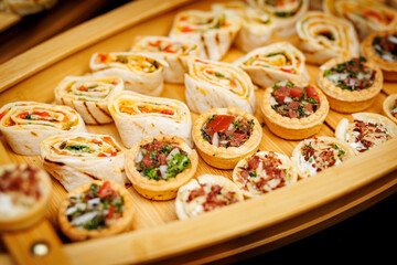 Assorted appetizer rolls and mini tarts on wooden tray