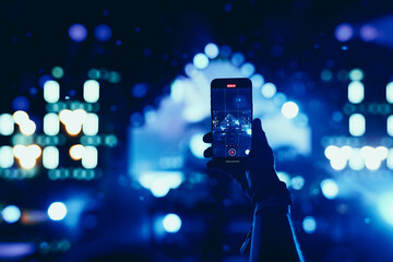 Hand holding smartphone recording live concert with blue lights