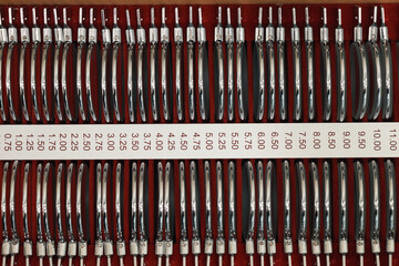 Set of metal optometry trial lenses arranged in rows on red background, each lens labeled with specific diopter value, used for vision testing and eye examinations in clinical settings © DragonImages