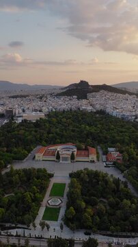 Slow panning drone shot of Zappeion Hall in Athens at sunrise with Lycabettus Hill in the background. Vertical