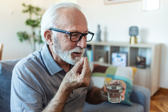 Senior man takes pill with glass of water in hand. Stressed mature man drinking sedated antidepressant meds. Man feels depressed, taking drugs.