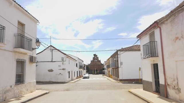 A walk along a main street in Navas de Tolosa (Ja&eacute;n, Andalusia). The view shows traditional white facades, balconies, and a church tower.