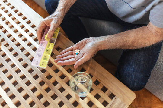 Pills, container and hands with medicine, table and healthcare for elderly person, medical and home. House, pharmaceutical and healthy for old man, closeup and storage for supplement of treatment.