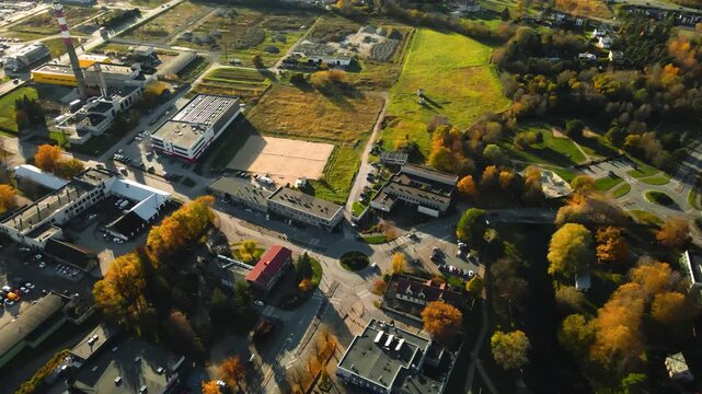 Aerial drone footage descending and flying lower upon a small urban town called Laagri in Estonia during autumn sunny day with trees that have yellow leaves around houses and roads with cars driving.