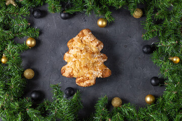 Festive christmas tree pastry with almonds surrounded by pine and baubles on dark stone background