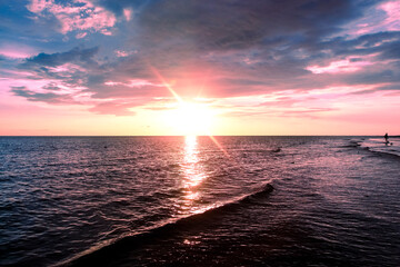 Breathtaking Pink and Purple Sunset Over the Ocean Horizon with Bright Sun Glare and Reflection on Rolling Waves. Dramatic Seascape Photography Background Featuring a Solitary Silhouette on the Beach