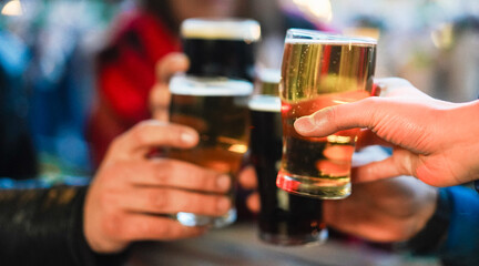 Young group of people having fun cheering with beer outdoor at pub restaurant - Winter lifestyle and party concept - Soft focus on right hand