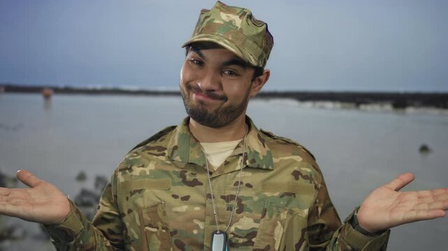 Young hispanic man in camouflage military uniform stands on street with both palms up shrug gesture facing the camera; uncertainty.