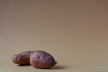 Two whole sweet potatoes on a brown background.