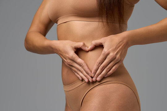 Fit woman forming heart shape with hands on her flat stomach in beige underwear
