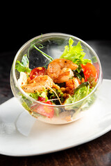 A gourmet shrimp salad served in a clear glass bowl on a white plate. The salad features grilled...