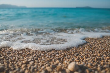Close-up of sandy pebble shoreline with foamy ocean waves and a soft blue horizon in the background