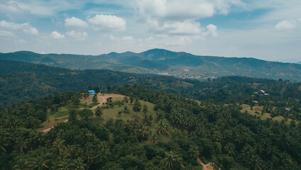 Fototapeta premium Aerial view of mountain range and valley surrounded by lush forests and coconut trees, showcasing summer's natural beauty