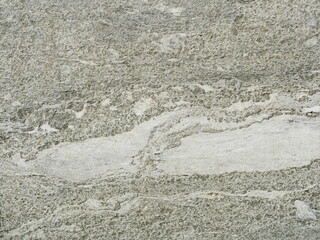 Granite-like stone surface in gray tones with rough texture and lighter inclusions. Close-up. Copyspace.