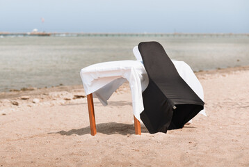 A table with a white tablecloth and a chair on the seashore. Place for a romantic date against a...