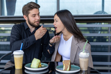 A man and a woman are sitting at a table, eating dessert and drinking together.