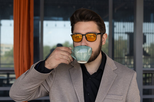 Man, drinking coffee, looks out rainy window, lost in thought